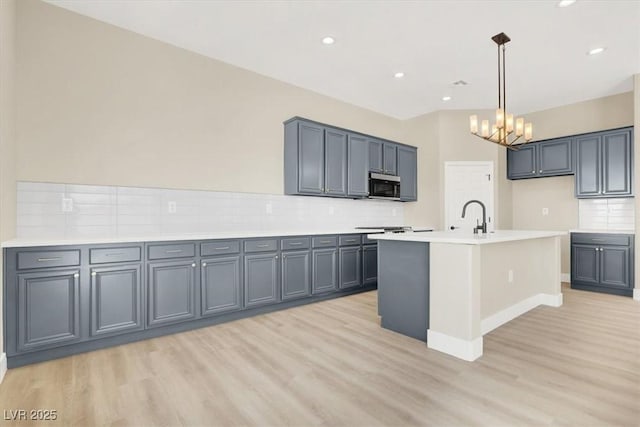 5908 Big Horn View St, North Las Vegas, NV 89031 - kitchen featuring stainless steel microwave, light wood-style floors, decorative backsplash, a chandelier, and light countertops