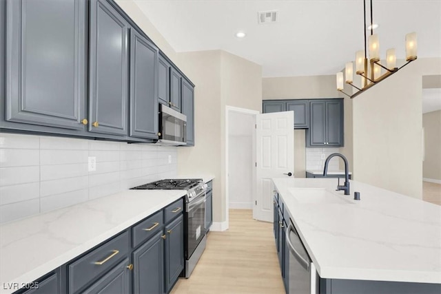 5908 Big Horn View St, North Las Vegas, NV 89031 - kitchen with appliances with stainless steel finishes, a center island with sink, backsplash, light wood-style flooring, and light stone counters