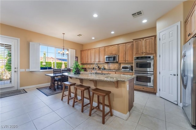 12276 Caminita Pl, Las Vegas, NV 89138 - kitchen with stainless steel appliances, a chandelier, a kitchen island with sink, light stone counters, and a breakfast bar