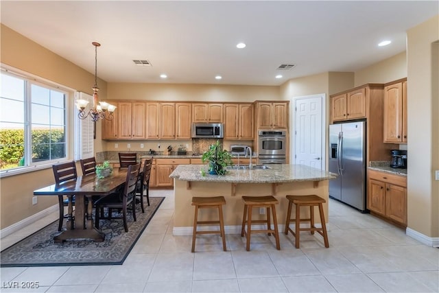 12276 Caminita Pl, Las Vegas, NV 89138 - kitchen featuring appliances with stainless steel finishes, a chandelier, a center island with sink, light stone countertops, and hanging light fixtures