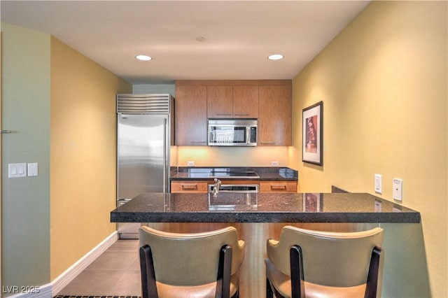 2000 Fashion Show Dr Unit 4105-4106, Las Vegas, NV 89109 - kitchen with appliances with stainless steel finishes, tile patterned flooring, brown cabinetry, a kitchen bar, and dark stone counters