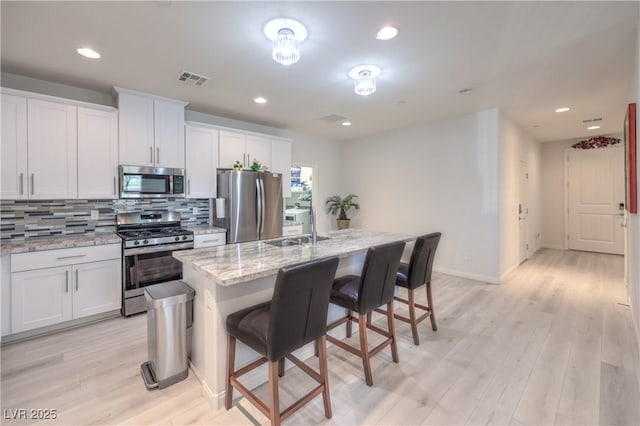 326 Zenith Crest St, Henderson, NV 89015 - kitchen with appliances with stainless steel finishes, decorative backsplash, a kitchen bar, light wood finished floors, and white cabinets