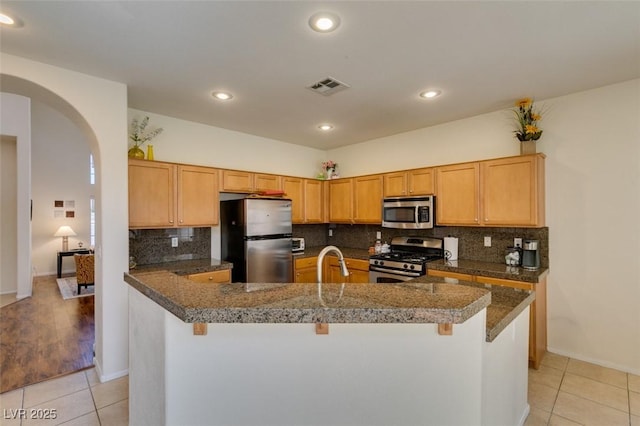 10952 Porto Foxi St, Las Vegas, NV 89141 - kitchen featuring appliances with stainless steel finishes, light tile patterned flooring, backsplash, arched walkways, and a breakfast bar area