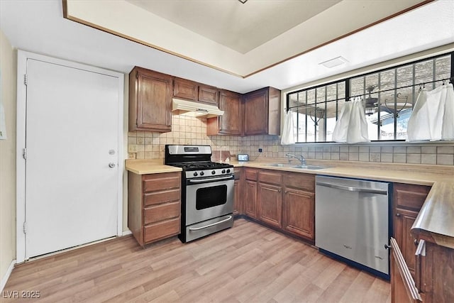 7113 Carrondale Way, Las Vegas, NV 89128 - kitchen featuring stainless steel appliances, under cabinet range hood, a raised ceiling, light wood-type flooring, and decorative backsplash