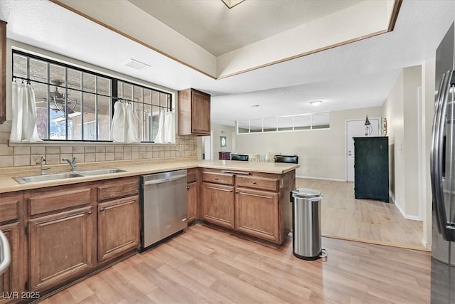 7113 Carrondale Way, Las Vegas, NV 89128 - kitchen featuring stainless steel appliances, brown cabinetry, a peninsula, light wood finished floors, and backsplash