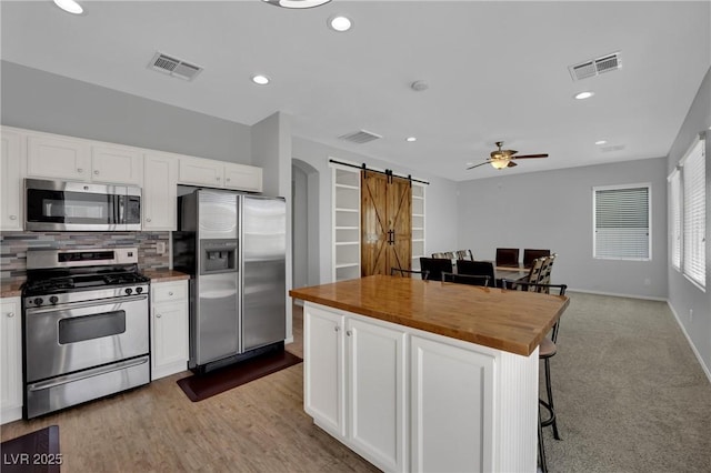 9131 Grand Sunburst Ct, Las Vegas, NV 89149 - kitchen with appliances with stainless steel finishes, a barn door, wooden counters, ceiling fan, and white cabinetry