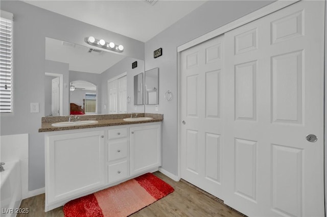 9131 Grand Sunburst Ct, Las Vegas, NV 89149 - bathroom featuring wood finished floors, double vanity, a bath, and a ceiling fan