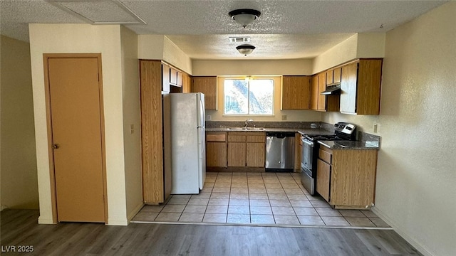 3412 Mercury St Unit I, North Las Vegas, NV 89030 - kitchen with appliances with stainless steel finishes, dark countertops, under cabinet range hood, brown cabinetry, and a textured ceiling