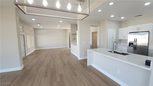2904 Bow Bridge Dr, Las Vegas, NV 89134 - kitchen with stainless steel fridge with ice dispenser, light wood-style flooring, recessed lighting, white cabinets, and light stone countertops