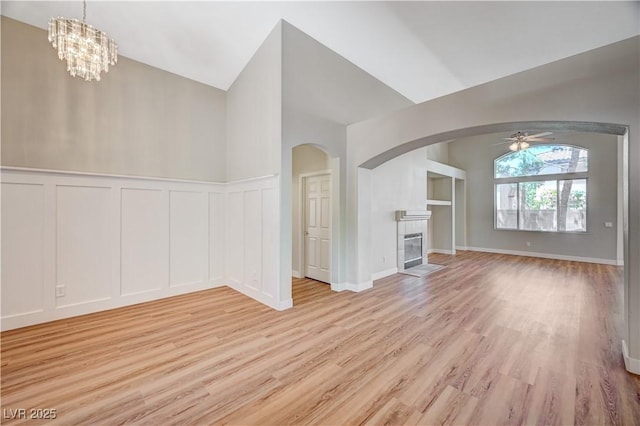 10198 Timber Willow Ave, Las Vegas, NV 89135 - unfurnished living room with a decorative wall, light wood finished floors, a tiled fireplace, arched walkways, and a ceiling fan