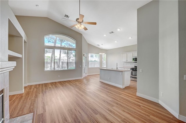 10198 Timber Willow Ave, Las Vegas, NV 89135 - unfurnished living room featuring ceiling fan, light wood-type flooring, a tiled fireplace, high vaulted ceiling, and a chandelier