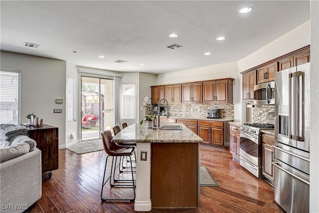 1717 Jake Andrew Ave, North Las Vegas, NV 89086 - kitchen with stainless steel appliances, dark wood-style flooring, a kitchen island with sink, a breakfast bar area, and backsplash