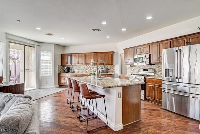 1717 Jake Andrew Ave, North Las Vegas, NV 89086 - kitchen with appliances with stainless steel finishes, decorative backsplash, a kitchen bar, a center island with sink, and light stone countertops