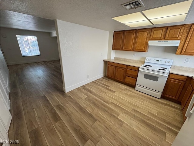 453 Las Casitas Way, Las Vegas, NV 89121 - kitchen with white range with electric cooktop, under cabinet range hood, brown cabinets, light wood-style floors, and a textured ceiling