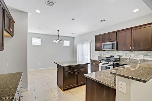 7263 Pepperbox Ave, Las Vegas, NV 89179 - kitchen with appliances with stainless steel finishes, dark stone counters, dark brown cabinetry, a center island, and backsplash