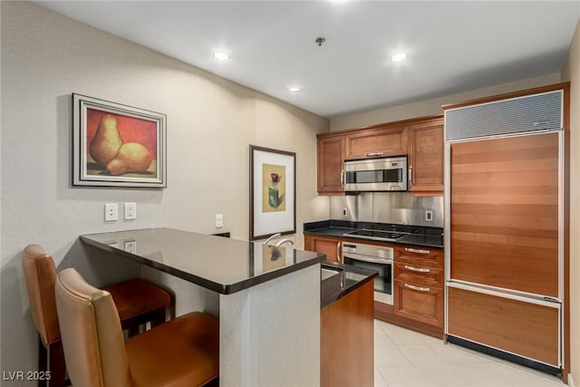 135 E Harmon Ave Unit 2702, Las Vegas, NV 89109 - kitchen featuring appliances with stainless steel finishes, a peninsula, brown cabinetry, dark countertops, and a kitchen breakfast bar