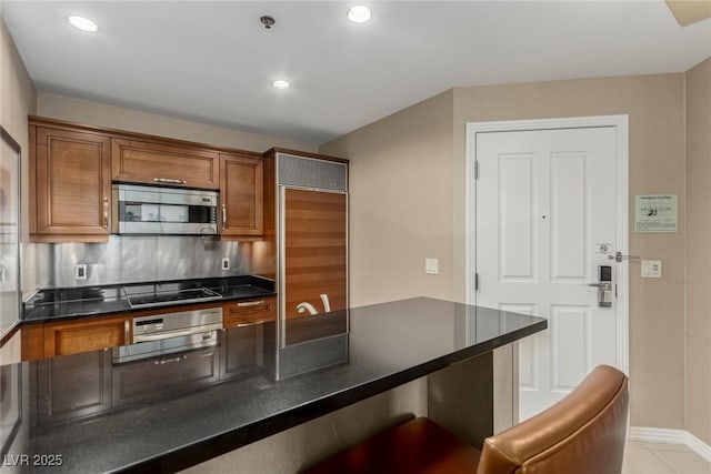 135 E Harmon Ave Unit 2702, Las Vegas, NV 89109 - kitchen featuring stainless steel microwave, dark countertops, black electric cooktop, brown cabinets, and a kitchen bar