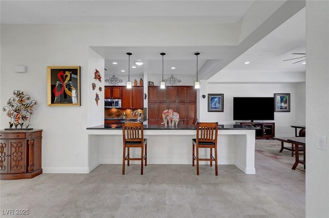 2779 Kindeace Ave, Henderson, NV 89044 - kitchen featuring dark countertops, a breakfast bar area, stainless steel microwave, a peninsula, and decorative light fixtures