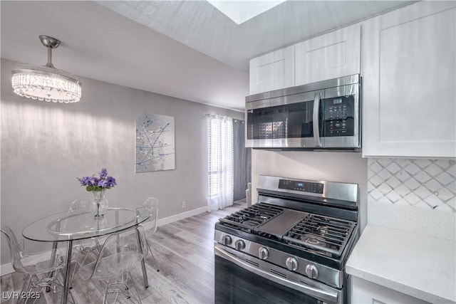 5219 Caliente St Unit 11, Las Vegas, NV 89119 - kitchen featuring appliances with stainless steel finishes, light wood-style floors, white cabinetry, decorative backsplash, and a chandelier