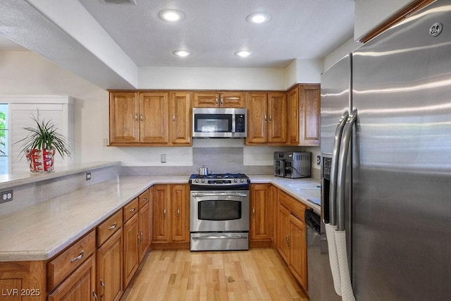 9357 Golden Timber Ln, Las Vegas, NV 89117 - kitchen with stainless steel appliances, brown cabinets, light wood-style flooring, light countertops, and recessed lighting