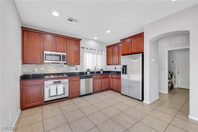 6678 Crystal Run Ln, Las Vegas, NV 89122 - kitchen featuring appliances with stainless steel finishes, separate washer and dryer, dark countertops, decorative backsplash, and arched walkways