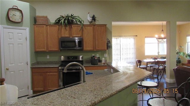 1504 Andrew David Ave, North Las Vegas, NV 89086 - kitchen featuring stainless steel appliances, brown cabinets, light stone countertops, and a kitchen breakfast bar