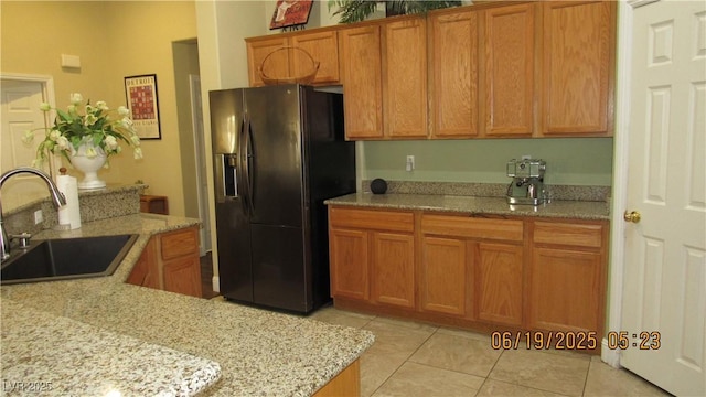 1504 Andrew David Ave, North Las Vegas, NV 89086 - kitchen with black refrigerator with ice dispenser, light tile patterned floors, brown cabinetry, and light stone countertops
