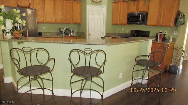 1504 Andrew David Ave, North Las Vegas, NV 89086 - kitchen featuring freestanding refrigerator, stove, a breakfast bar area, brown cabinets, and light stone countertops