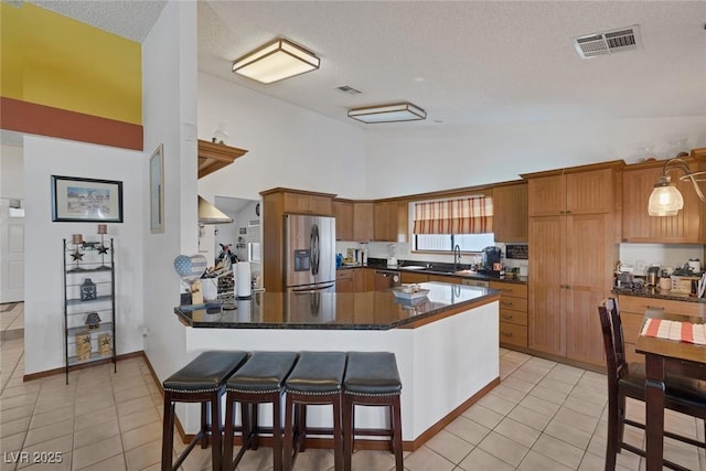 9100 Shelter Cove Ct, Las Vegas, NV 89117 - kitchen with stainless steel fridge with ice dispenser, light tile patterned floors, dark countertops, high vaulted ceiling, and a breakfast bar area