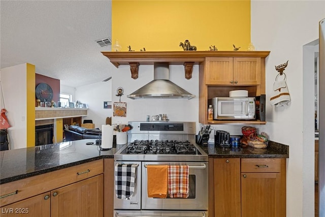 9100 Shelter Cove Ct, Las Vegas, NV 89117 - kitchen with stainless steel gas stove, wall chimney exhaust hood, dark stone counters, vaulted ceiling, and a fireplace