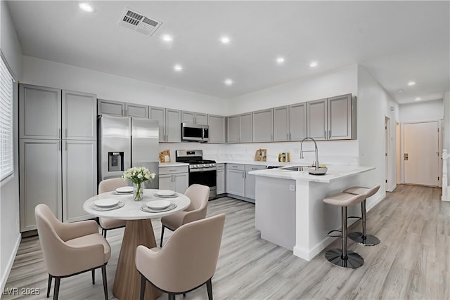 6346 Azurelyn Ave, Las Vegas, NV 89122 - kitchen featuring stainless steel appliances, gray cabinetry, a peninsula, a kitchen breakfast bar, and light wood finished floors