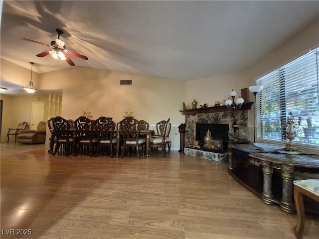 dining space featuring a ceiling fan, wood finished floors, lofted ceiling, and a stone fireplace