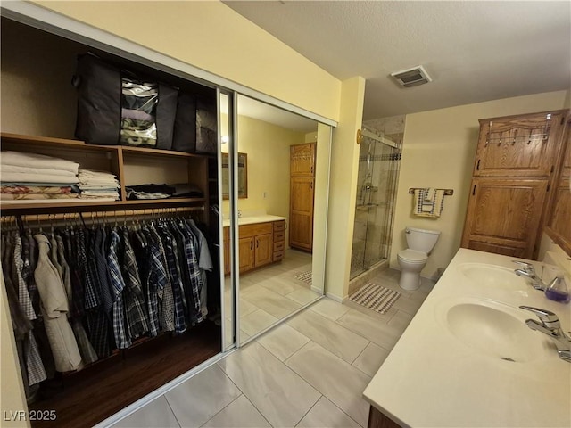 bathroom featuring a stall shower, double vanity, a walk in closet, and tile patterned flooring