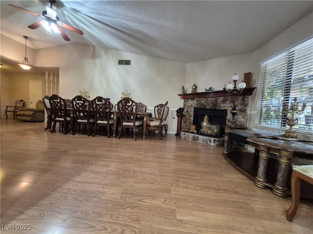 dining area featuring wood finished floors, ceiling fan, a fireplace, vaulted ceiling, and a textured ceiling