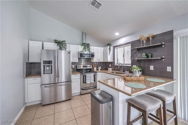 905 Smith St, Las Vegas, NV 89108 - kitchen featuring stainless steel appliances, decorative backsplash, lofted ceiling, a peninsula, and white cabinets