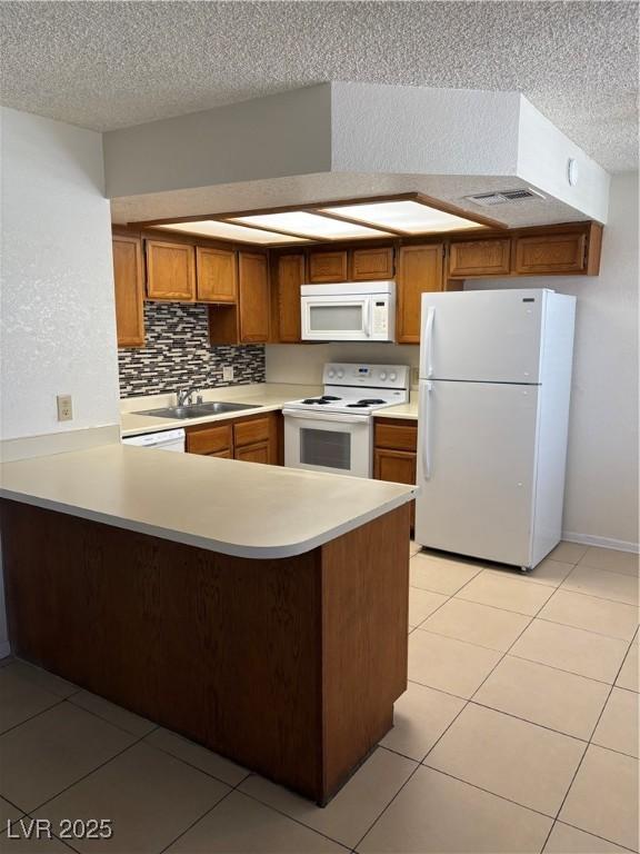 925 Falconhead Ln Unit 102, Las Vegas, NV 89128 - kitchen featuring white appliances, a textured ceiling, brown cabinetry, light countertops, and a peninsula