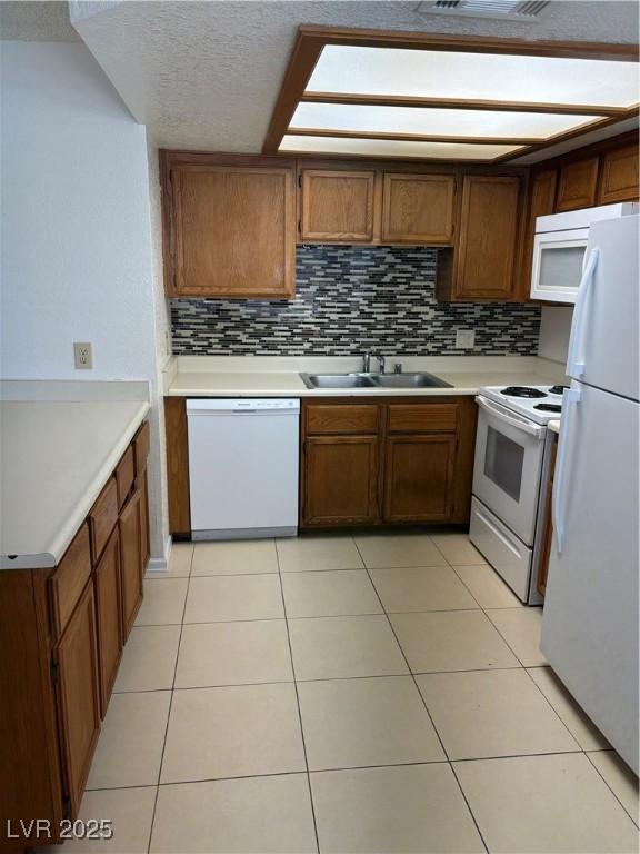 925 Falconhead Ln Unit 102, Las Vegas, NV 89128 - kitchen featuring white appliances, tasteful backsplash, brown cabinetry, light countertops, and a textured ceiling