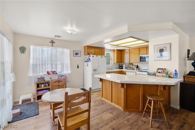 2730 Banyon St, Pahrump, NV 89048 - kitchen with white appliances, light wood-style flooring, a peninsula, and tile countertops