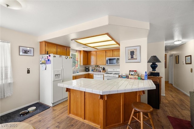 2730 Banyon St, Pahrump, NV 89048 - kitchen with white appliances, light wood-style floors, a breakfast bar, brown cabinets, and tile counters