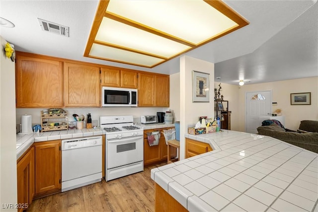 2730 Banyon St, Pahrump, NV 89048 - kitchen with white appliances, light wood-style floors, tile counters, open floor plan, and a peninsula