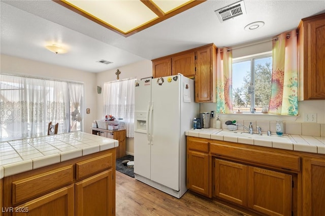 2730 Banyon St, Pahrump, NV 89048 - kitchen with white fridge with ice dispenser, light wood finished floors, and brown cabinetry