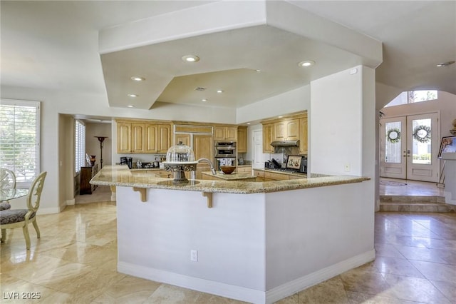 9905 Fox Springs Dr, Las Vegas, NV 89117 - kitchen featuring double oven, light stone countertops, a kitchen bar, french doors, and under cabinet range hood