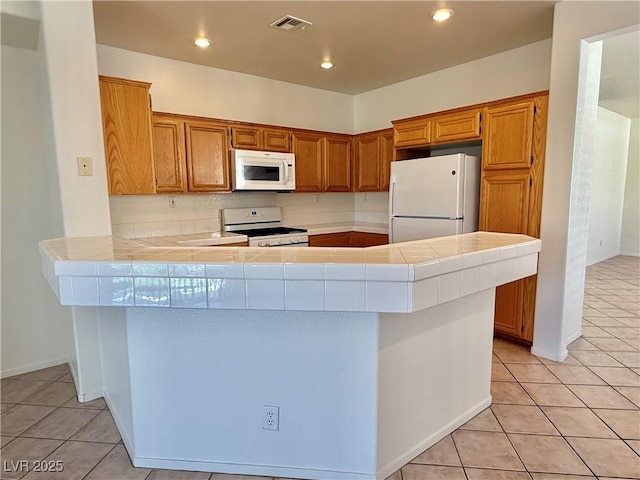 338 Brilliant Summit Cir, Henderson, NV 89052 - kitchen with white appliances, tile counters, light tile patterned floors, a peninsula, and brown cabinetry