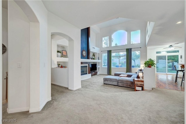 8812 Glenistar Gate Ave, Las Vegas, NV 89143 - living room with carpet floors, a glass covered fireplace, a towering ceiling, ceiling fan, and built in features
