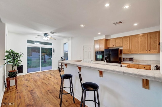 8812 Glenistar Gate Ave, Las Vegas, NV 89143 - kitchen with black appliances, a kitchen breakfast bar, tile counters, recessed lighting, and a peninsula