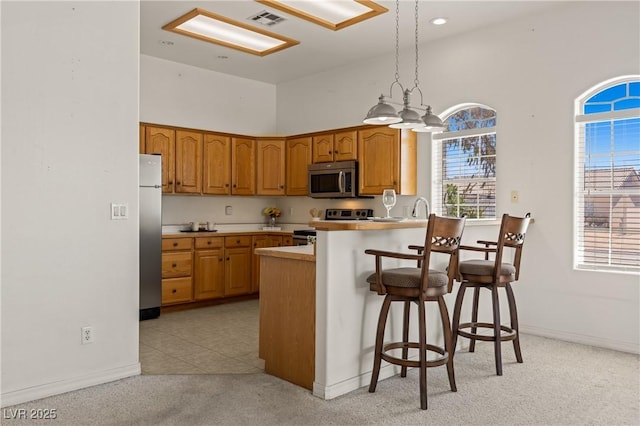 467 Muddy Peak Ct, Overton, NV 89040 - kitchen with stainless steel appliances, brown cabinetry, a peninsula, plenty of natural light, and a towering ceiling
