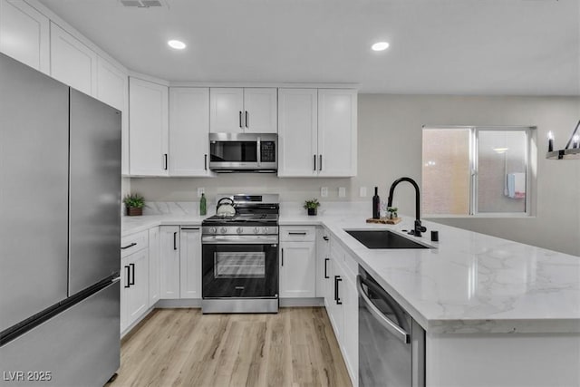 10373 Midnight Iris St, Las Vegas, NV 89183 - kitchen with stainless steel appliances, a peninsula, light wood finished floors, white cabinetry, and recessed lighting
