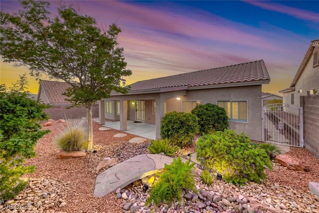 1643 Silver Slipper Ave, Henderson, NV 89002 - back of house at dusk featuring a tiled roof, stucco siding, a patio area, and a gate