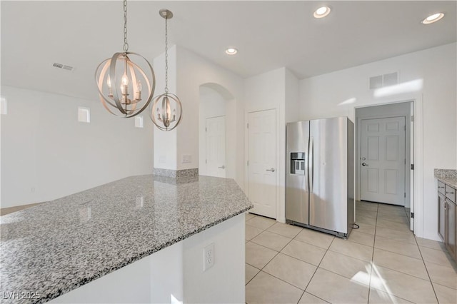 7775 Tyrell Peaks St, Las Vegas, NV 89139 - kitchen with stainless steel refrigerator with ice dispenser, a chandelier, light stone counters, light tile patterned floors, and arched walkways