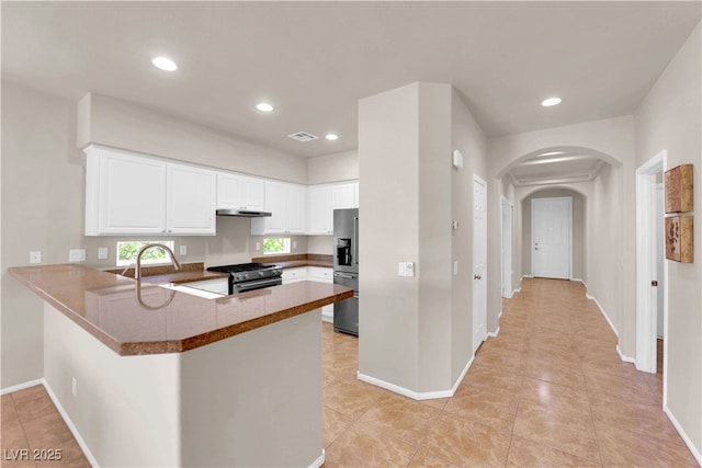 11139 Zarod Rd, Las Vegas, NV 89135 - kitchen featuring appliances with stainless steel finishes, a peninsula, arched walkways, under cabinet range hood, and white cabinetry